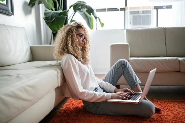 A woman sits on the floor while using a laptop.